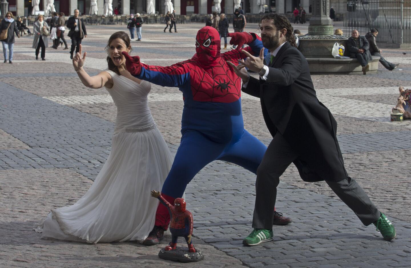 A bride and groom pose for photographs with a street performer dressed as a portly Spiderman in Plaza Mayor in Madrid.