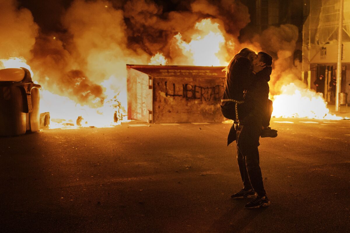 A couple kiss in front of a barricade set on fire by demonstrators during clashes with police following a protest condemning the imprisonment of rap singer Pablo Hasél in Barcelona, Spain, on Feb. 18, 2021. Hasél was convicted of insulting the Spanish monarchy and praising terrorist violence. (AP Photo/Emilio Morenatti)