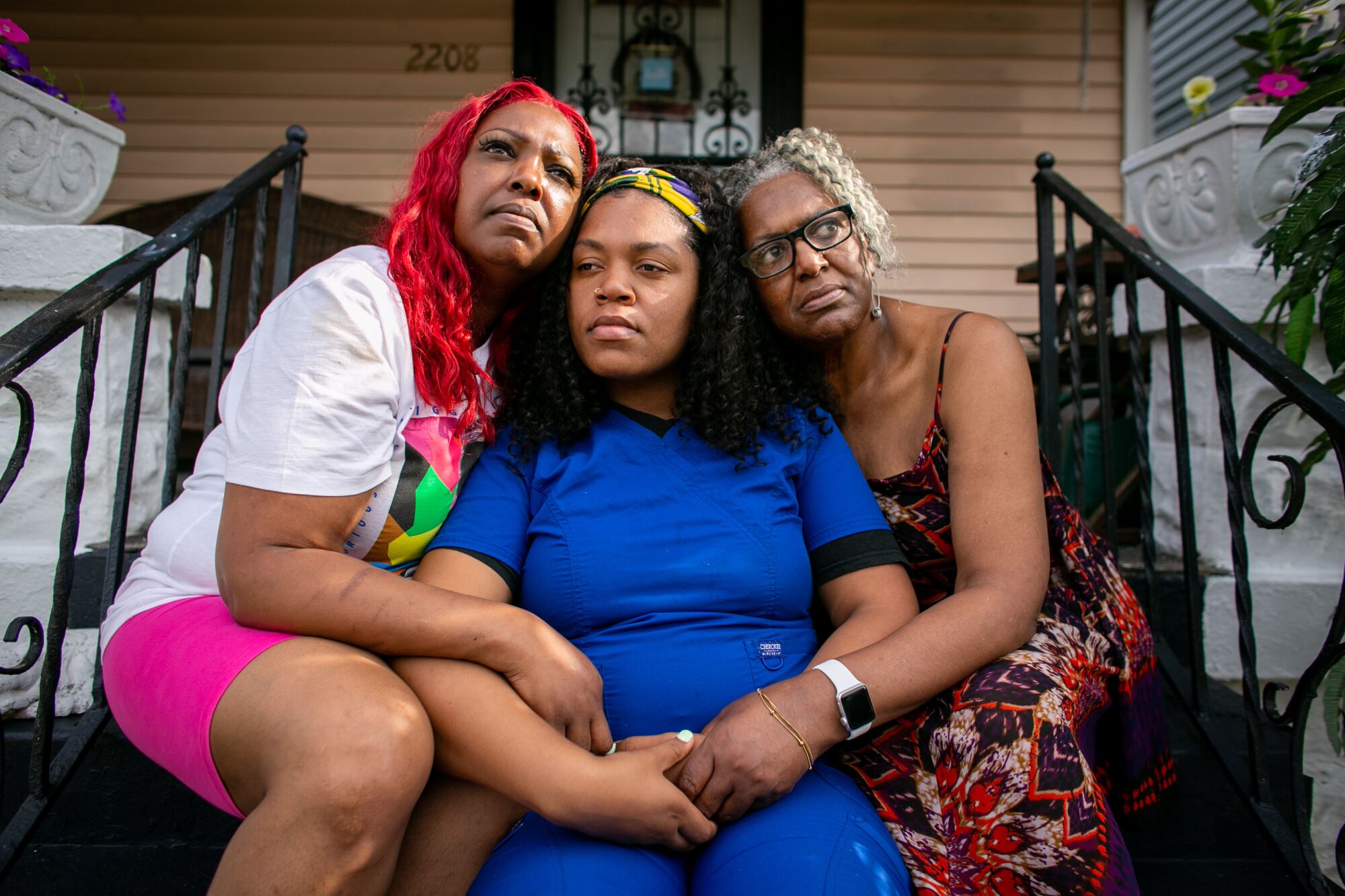 Three women embrace as they sit on a front porch.
