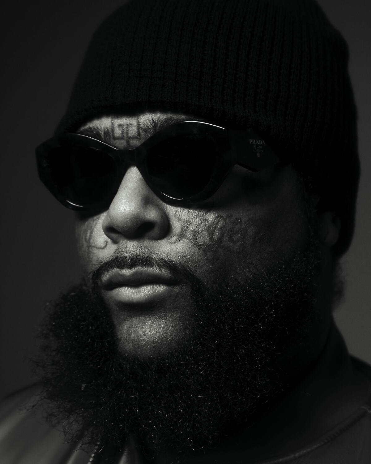 black and white photo of a man with face tattoos wearing sunglasses and a black beanie