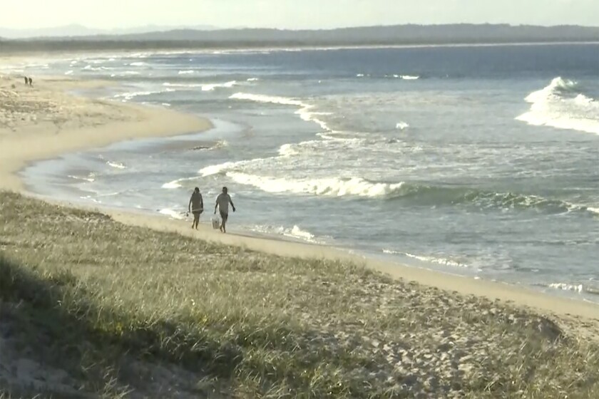 In this image made from a video, people walk along a beach in Tuncurry, Australia, Tuesday, May 18, 2021. A surfer was killed by a shark on Tuesday, police said. The man, aged in his 50s, had been surfing off Forster, 220 kilometers (137 miles) north of Sydney, when he was attacked late in the morning, a police statement said. (Australian Broadcasting Corporation via AP)