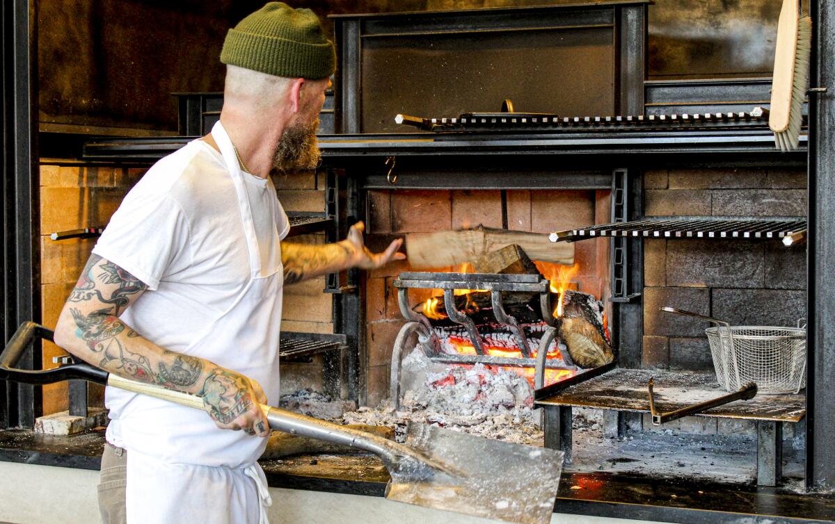 A chef throws wood into a hearth
