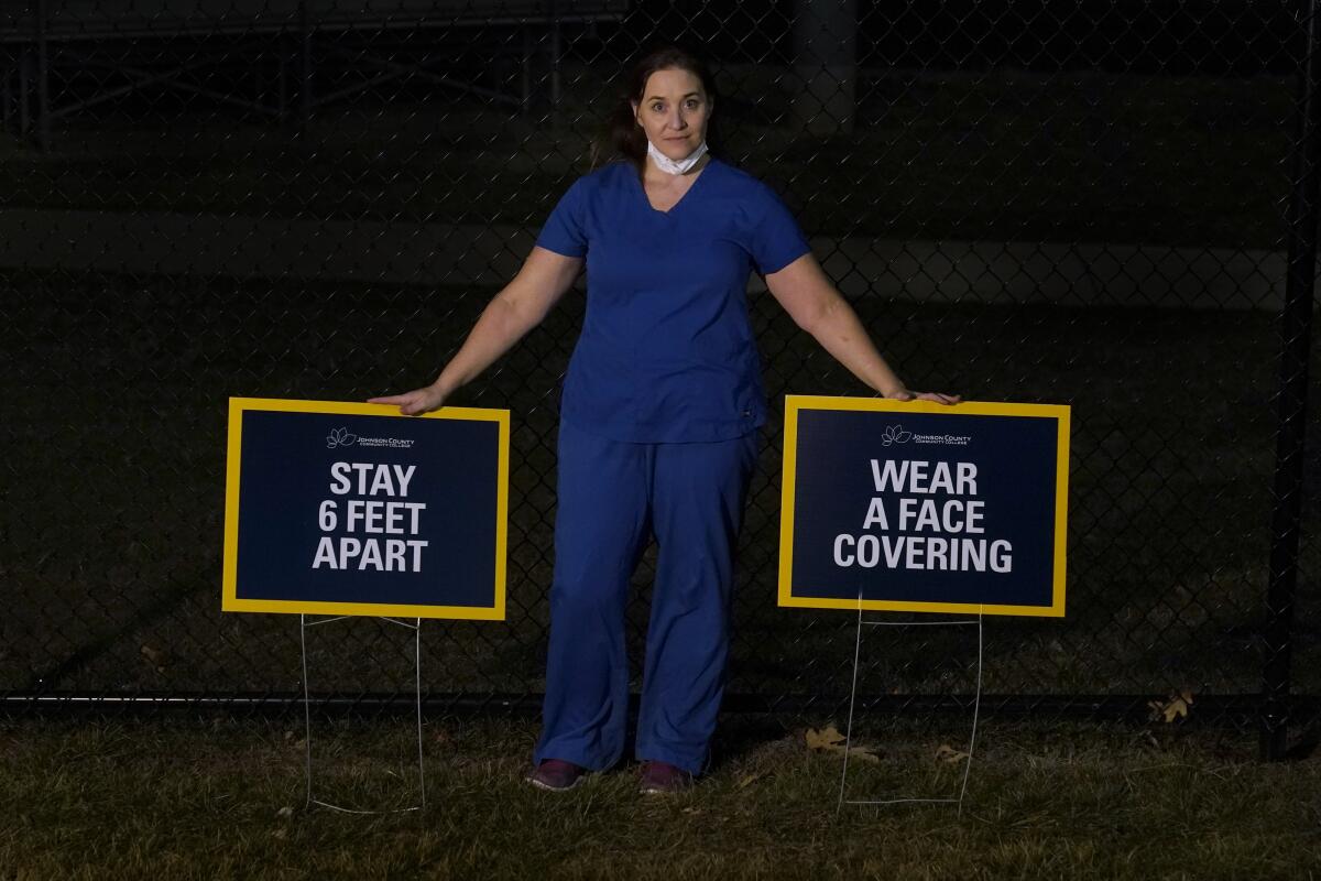 Emergency room nurse L'Erin Ogle poses with coronavirus signs after getting off a 12-hour shift at a nearby hospital where she works Monday, March 8, 2021, in Overland Park, Kan. After a year of working long hours taking care of COVID-19 patients, Ogle feels obligated to speak out when she sees misinformation related to the pandemic in her community. (AP Photo/Charlie Riedel)