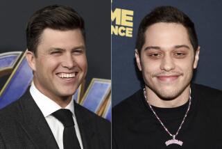 Colin Jost on the left wearing a black suit and tie, Pete Davidson on the right wearing a black shirt and a necklace