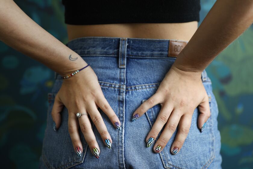 A person holds their manicured nails against their jeaned buttocks.