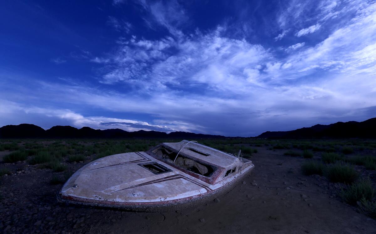 A powerboat rests on the floor of a dry lakebed. 