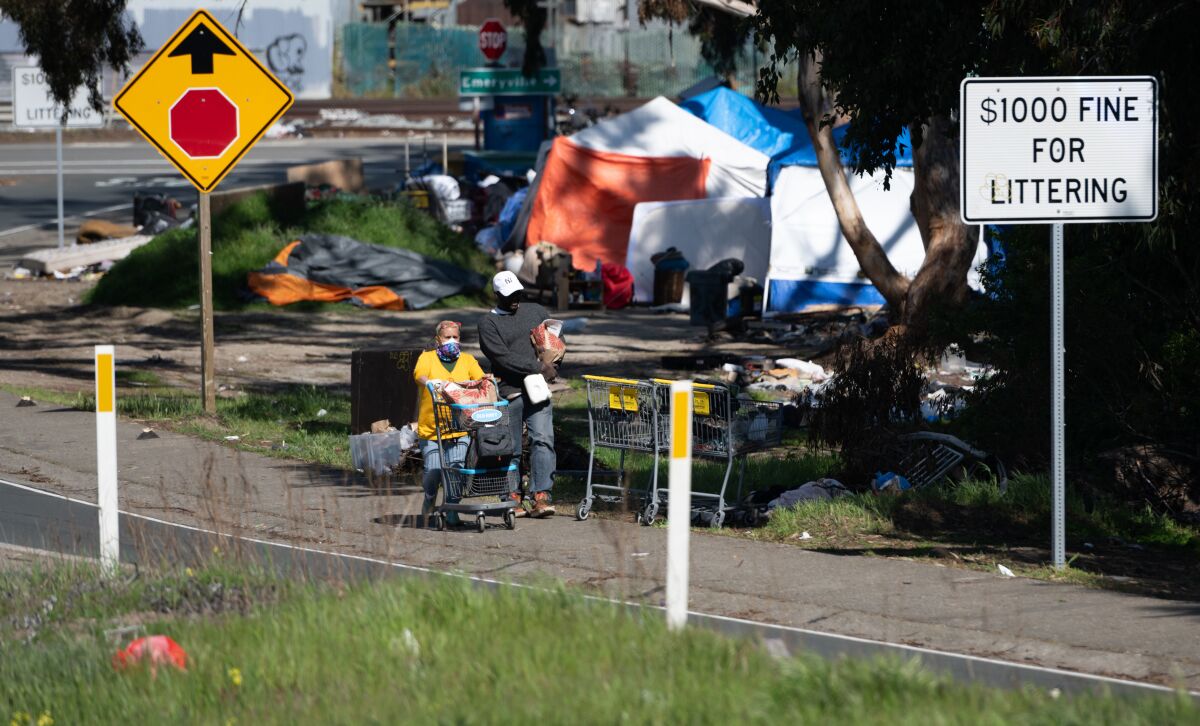 Two people in masks walk on a path in front of tents.