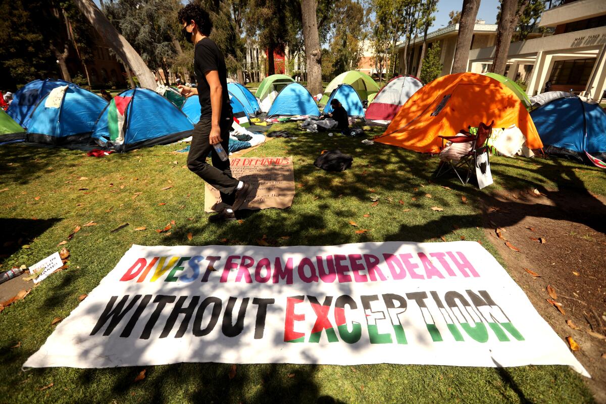 A sign on the ground near a tent encampment reads "Divest from queer death without exception."