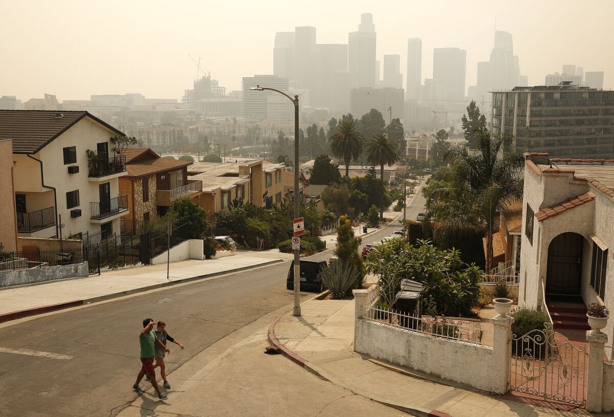 Alli Coyler and Luis Garcia walk under smoky skies along Figueroa Terrace near downtown L.A. on Monday.