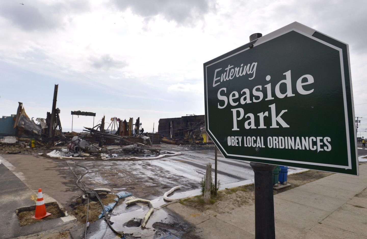 A sign for Seaside Park stands undamaged as firefighters continue working to extinguish embers after a fire destroyed dozens of businesses and attractions along the Jersey Shore boardwalk.