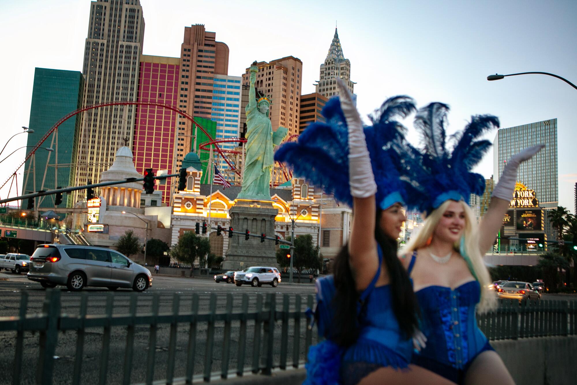 Two Vegas showgirls in blue outfits and feathered hats raise their arms in the air on the Strip