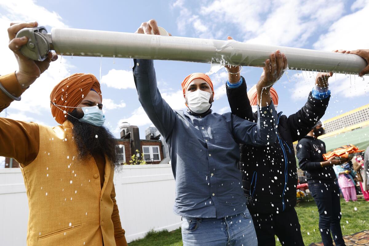 Jasbir Singh, left, and Vijay Singh wash a flagpole with milk as part of a ceremonial changing of the Sikh flag during Vaisakhi celebrations at Guru Nanak Darbar of Long Island, Tuesday, April 13, 2021 in Hicksville, N.Y. Sikhs across the United States are holding toned-down Vaisakhi celebrations this week, joining people of other faiths in observing major holidays cautiously this spring as COVID-19 keeps an uneven hold on the country. (AP Photo/Jason DeCrow)