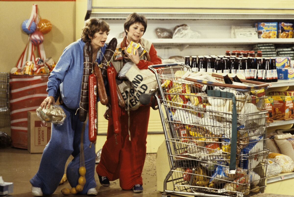 two women push a cart full of groceries 