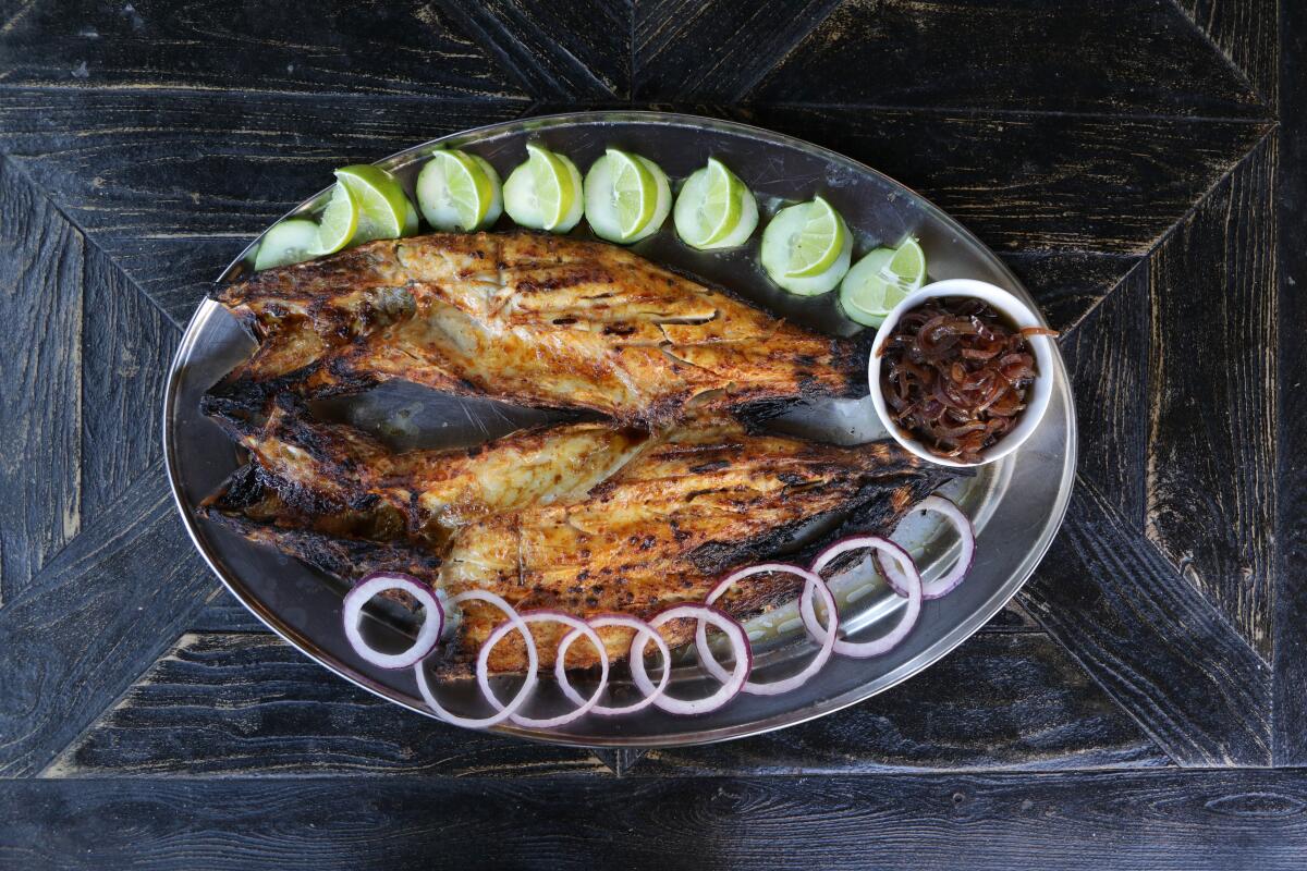 Pescado zarandeado is a whole butterflied fish, served on an oval platter with sliced limes, raw onion rings and salsa