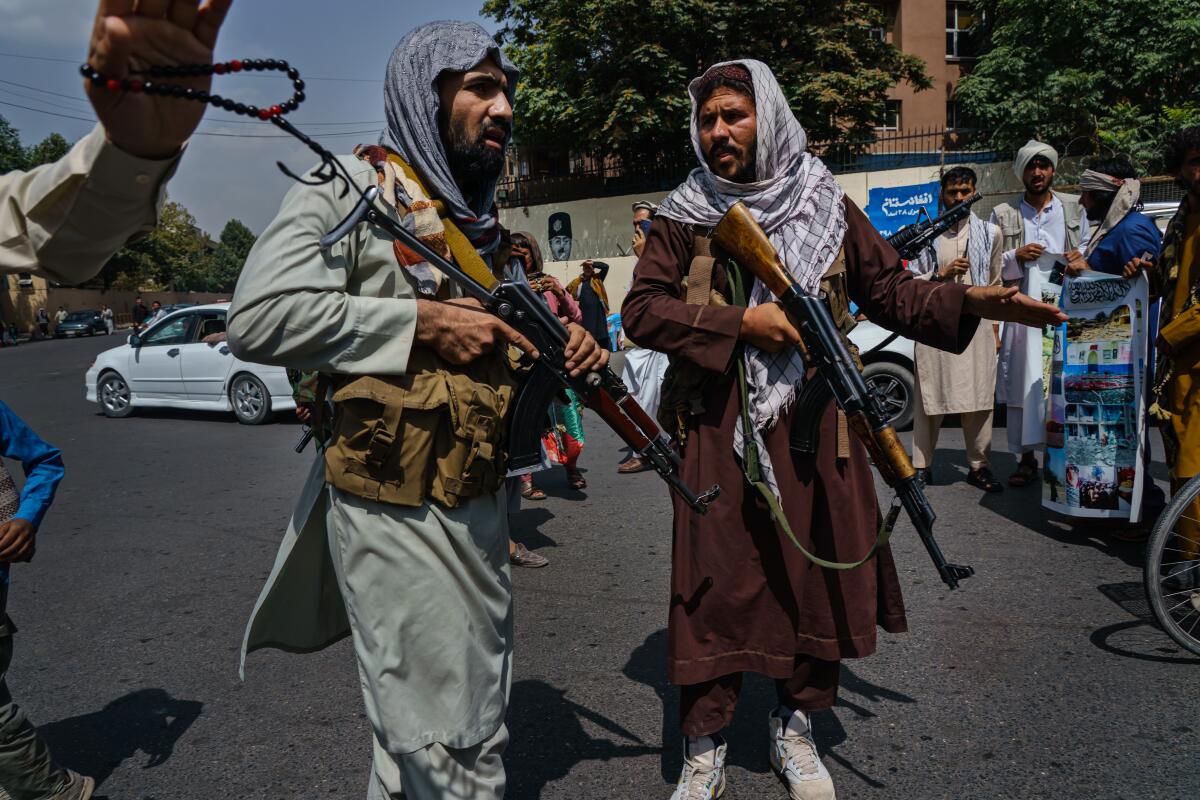 Two Taliban fighters with rifles talk in the street