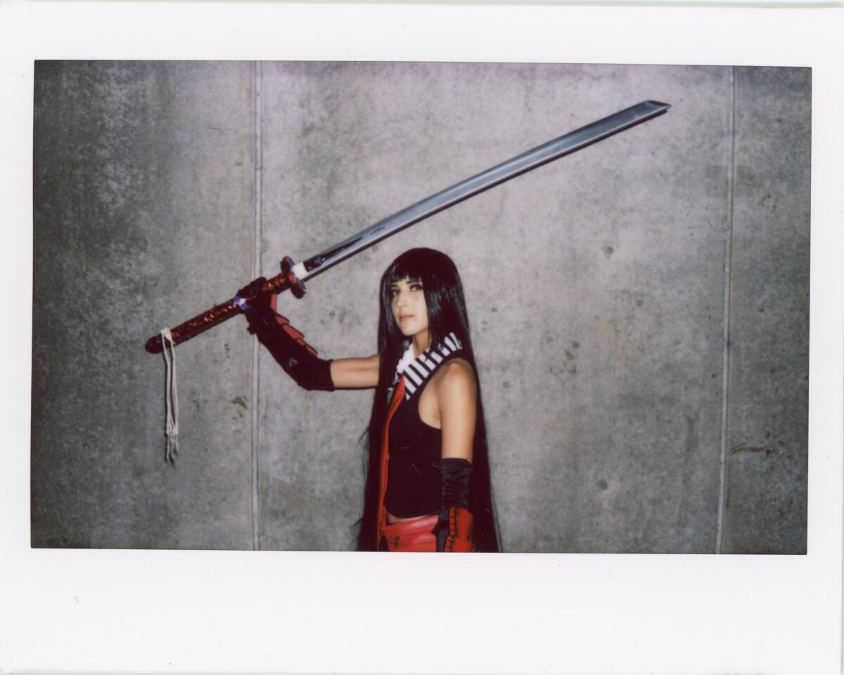 A woman with long straight dark hair holds a giant sword over her head.