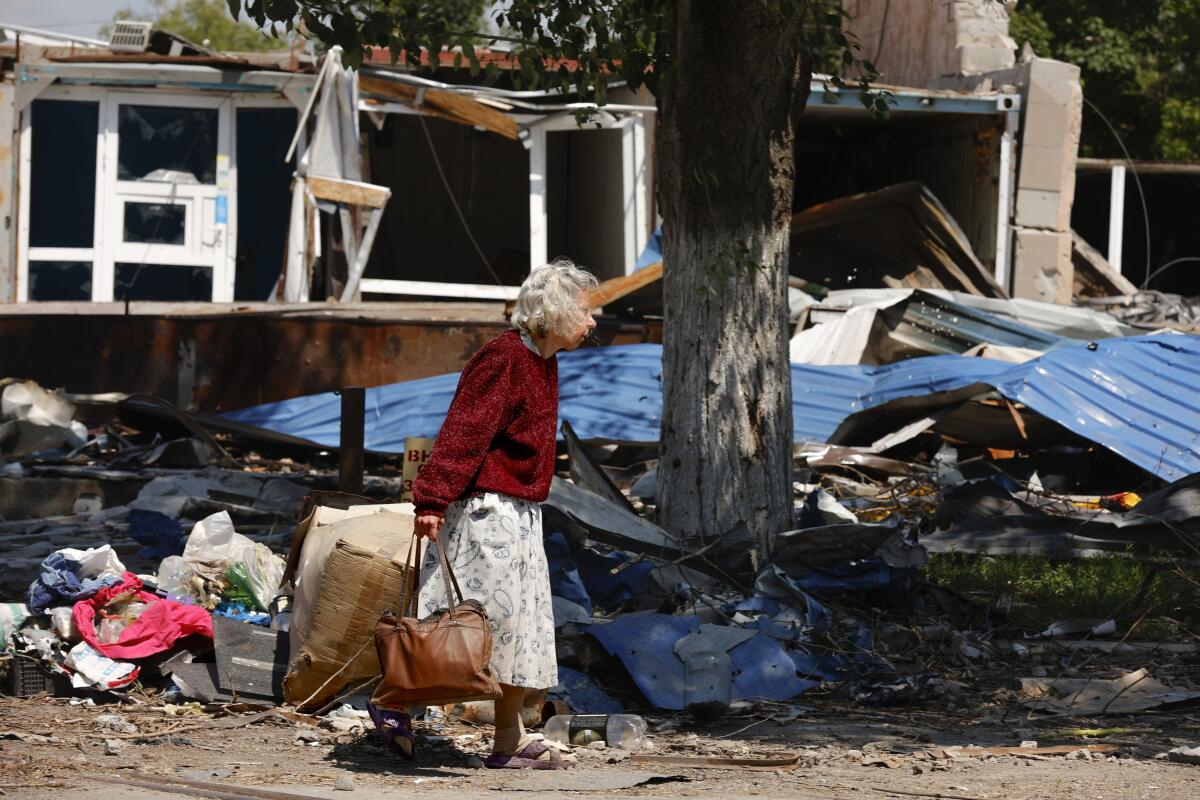 A woman carries a bag past destroyed homes in Mariupol.