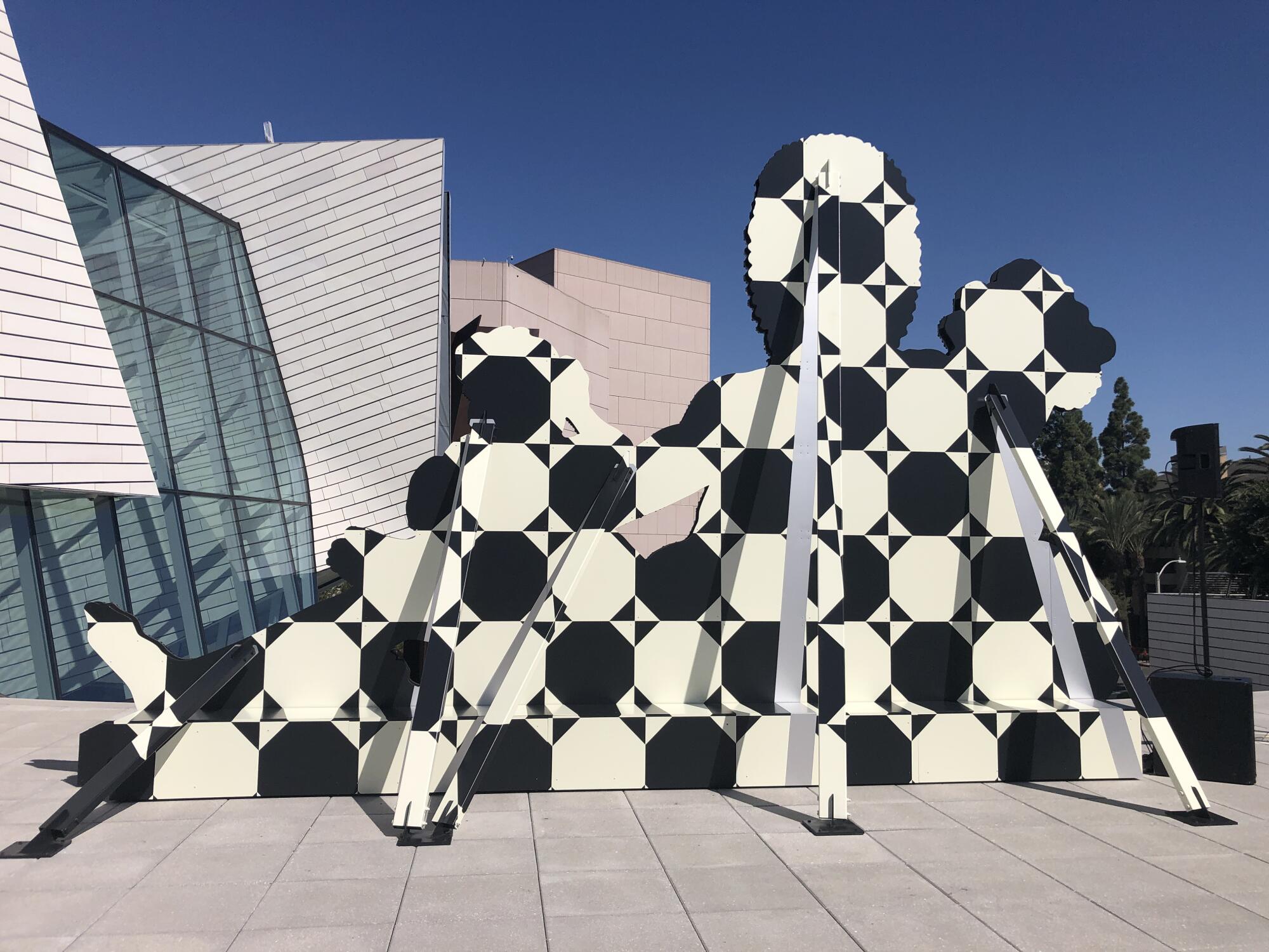 The outline of a human figure is rendered in a black and white geometric pattern on aluminum, supported by a scaffold. 