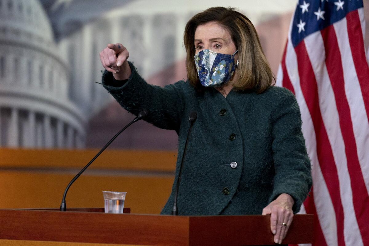 Nancy Pelosi, wearing a face mask, stands at a lectern.