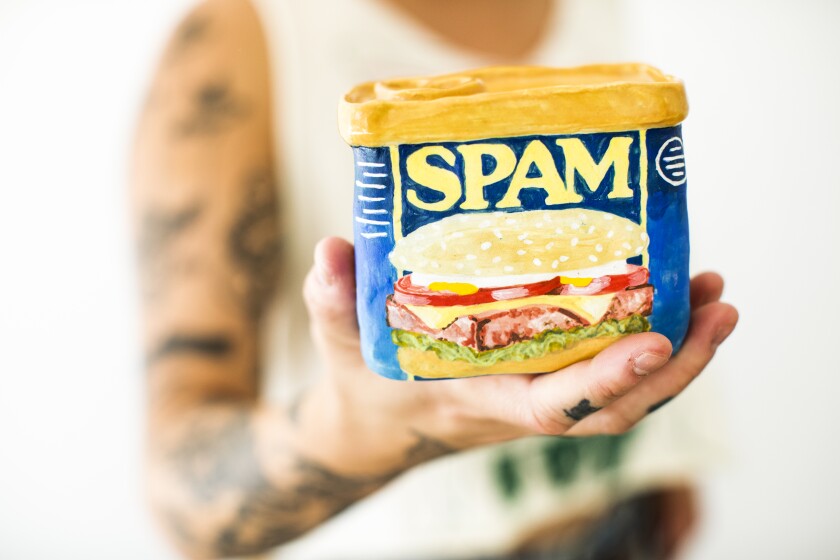 A closeup of a hand holding a ceramic interpretation of a tin of Spam