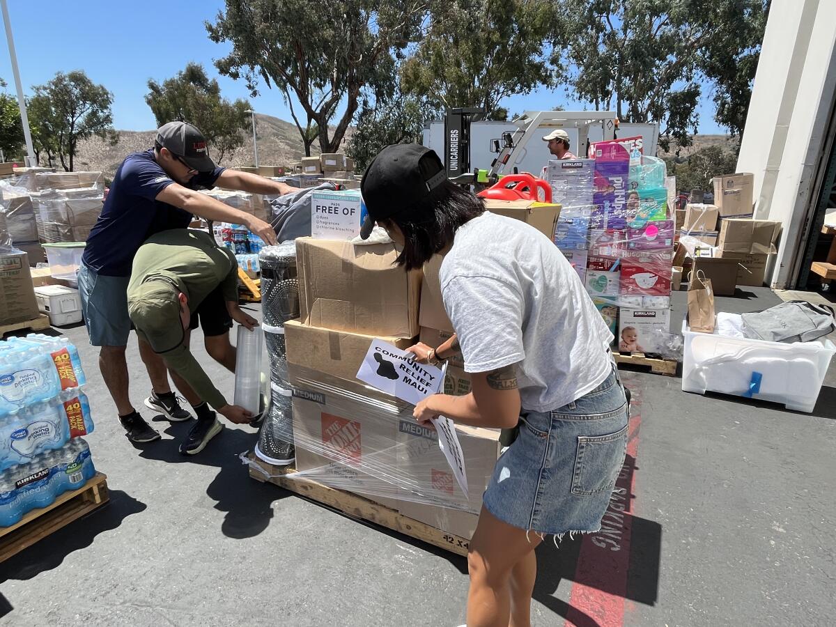 People wrap plastic around a pallet loaded with boxes.