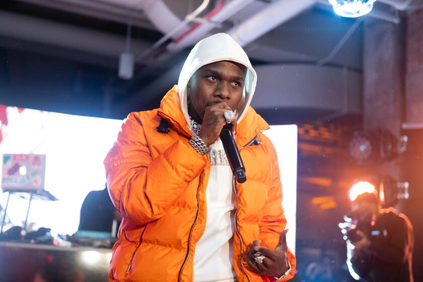 A man in an orange winter coat and white hoodie holding a microphone