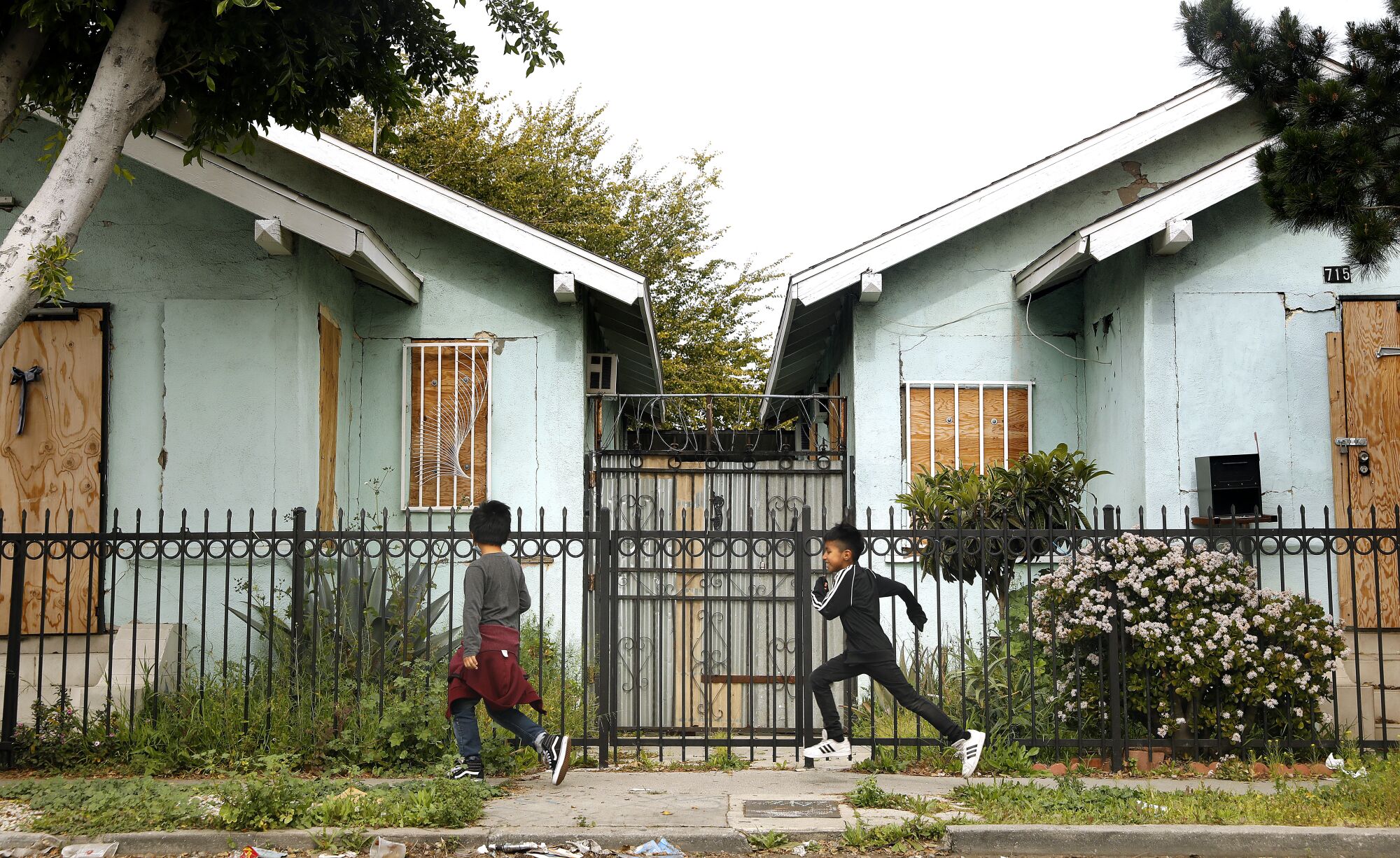 Deux enfants passent devant une clôture métallique et enferment des maisons 
