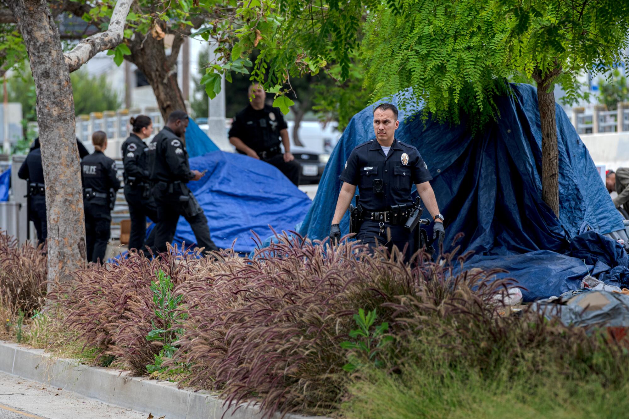 Police officers walk among tents in a homeless encampment.