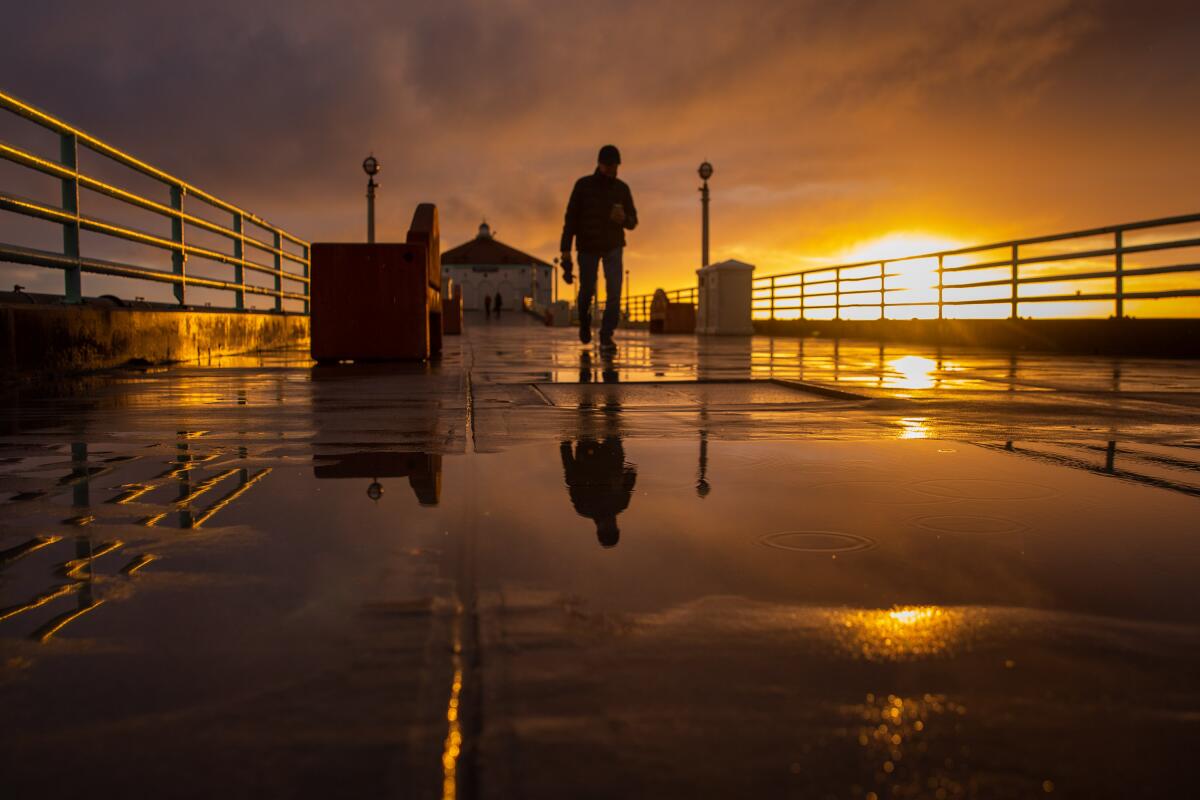 People walk on the Manhattan Beach Pier with the sun setting in the background.
