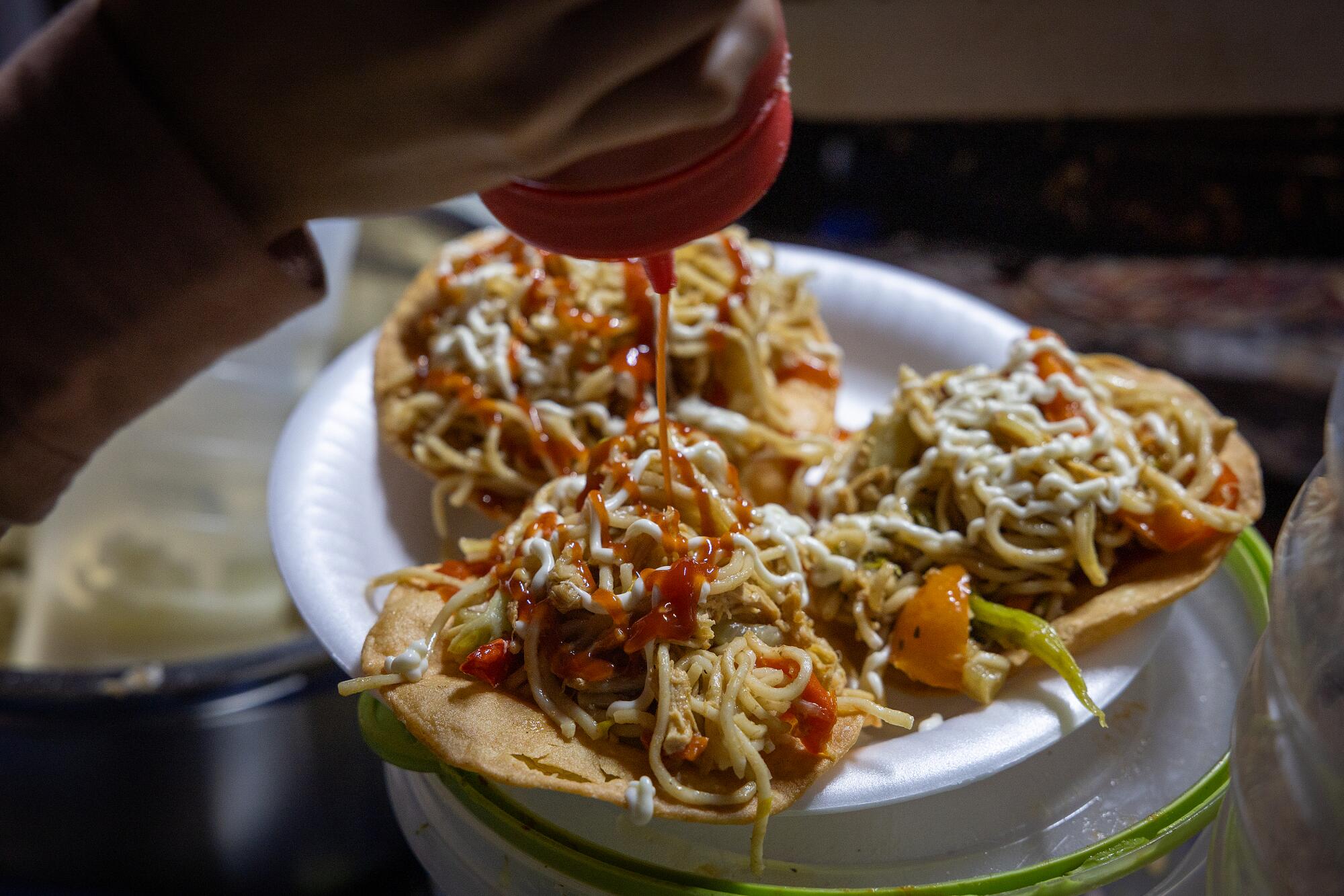 Yesenia Tunay pours mayonnaise and hot sauce on tostadas topped with chow mein at the Guatemalan Night Market.