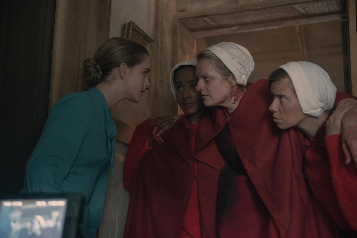 A woman in blue leans in to speak to an injured woman in red being carried by two others.