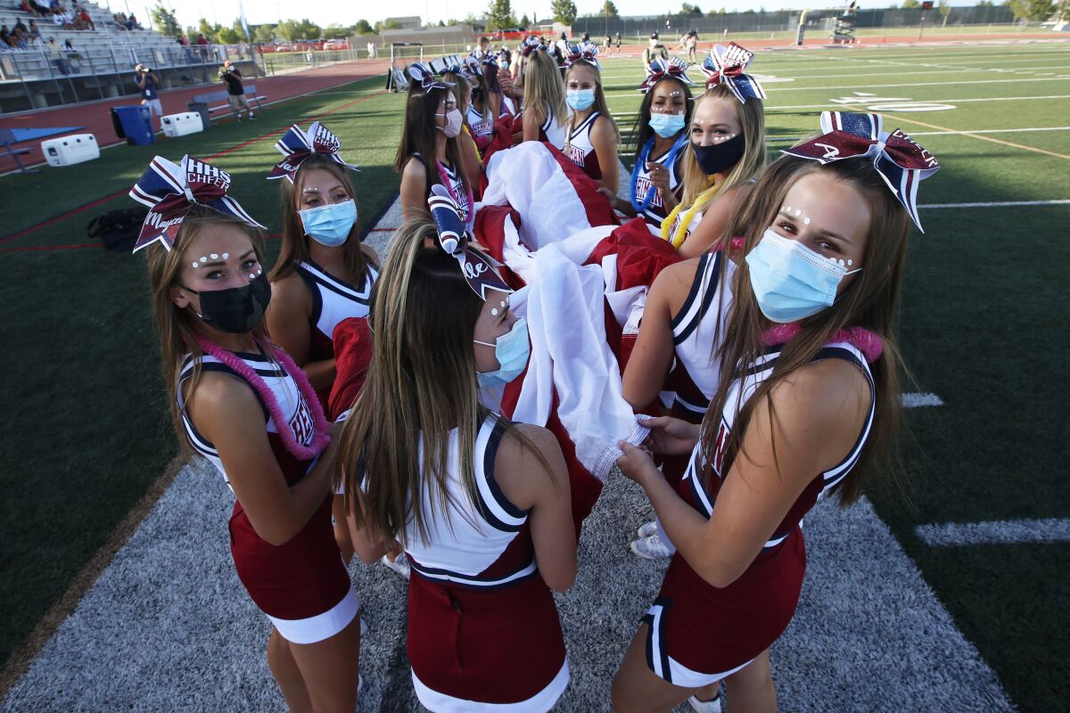 Herriman cheerleaders carry the American flag before the start of a high school football game against Davis, on Thursday, Aug. 13, 2020, in Herriman, Utah. Utah is among the states going forward with high school football this fall despite concerns about the ongoing COVID-19 pandemic that led other states and many college football conferences to postpone games in hopes of instead playing in the spring. (AP Photo/Rick Bowmer)