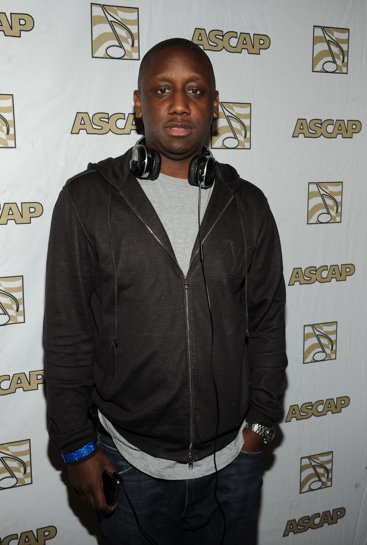 A man in a dark hoodie poses with headphones draped around his neck