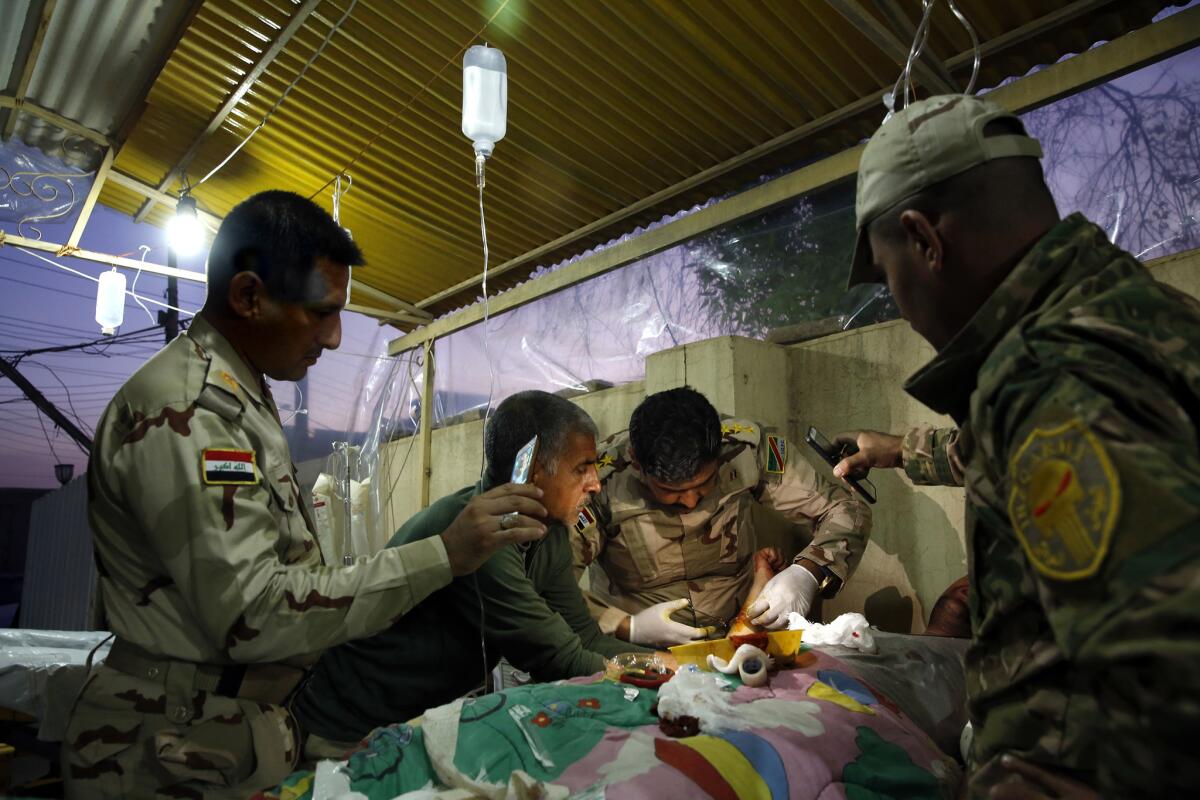 Capt. Osama Fuad Rauf works on a patient as others hold a cellphone for additional light at the Iraqi army’s 9th Armored Division medical clinic.