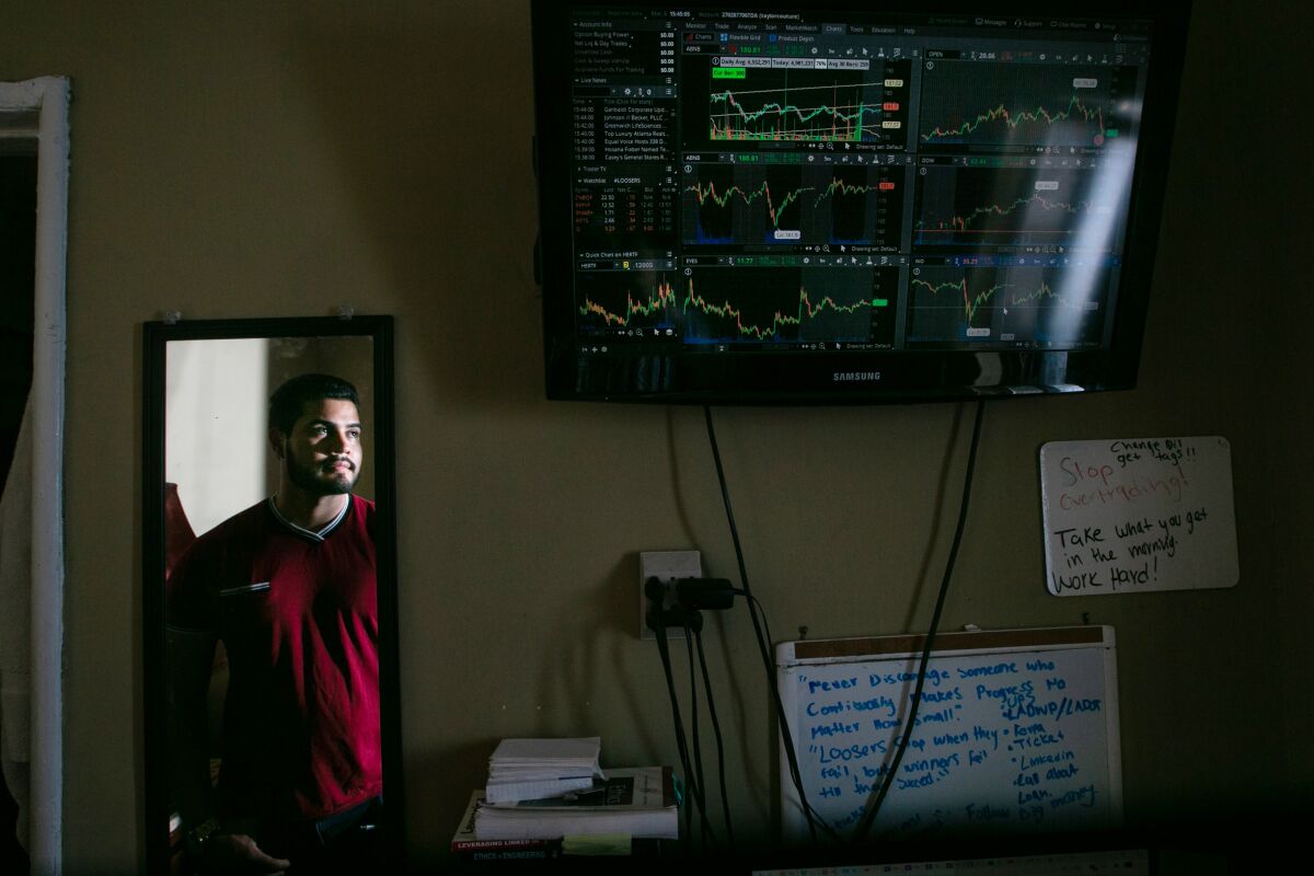 Royer Levith Elvir is reflected in a mirror near a TV screen that shows stock charts.