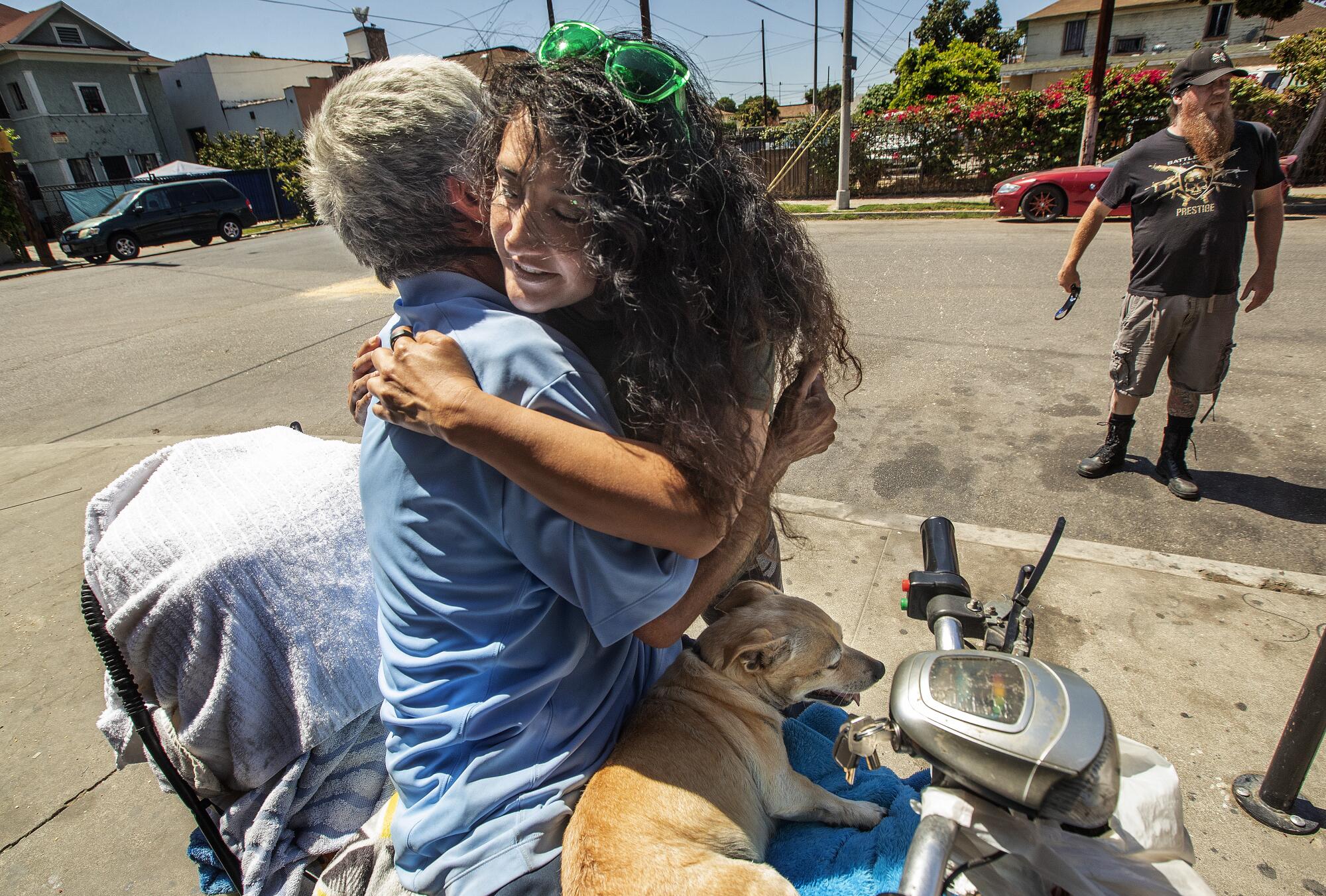 Gloria Hurtado hugs her father, Augustine, at his homeless encampment in South Los Angeles after delivering a new scooter.