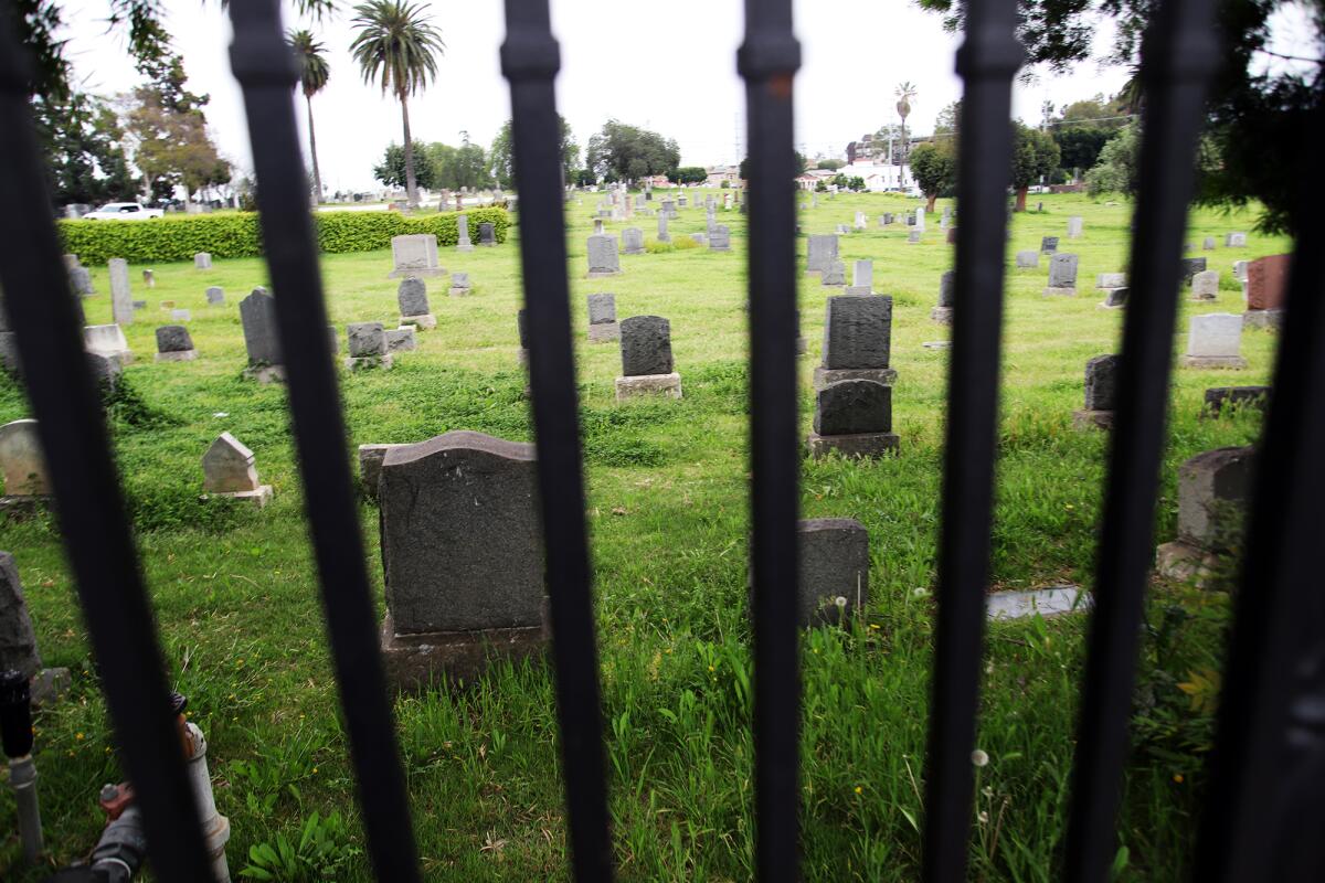 A view of gravestones in a cemetery through an iron fence