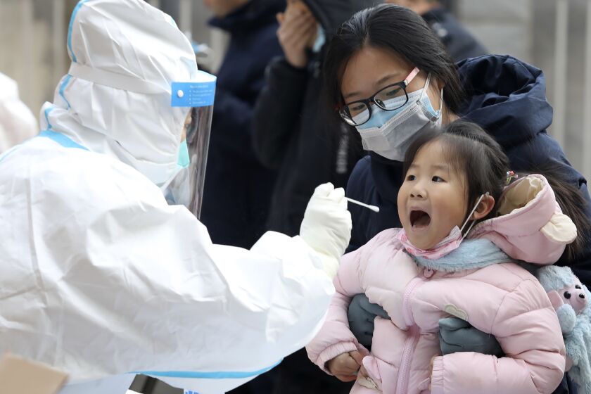 In this photo released by China's Xinhua News Agency, a worker in a protective suit takes a swab from a child for a coronavirus test in Shijiazhuang in northern China's Hebei Province, Monday, Jan. 12, 2021. Lockdowns have been expanded and a major political conference postponed in a province next to Beijing that is the scene of China's most serious recent COVID-19 outbreak. (Liang Zidong/Xinhua via AP)