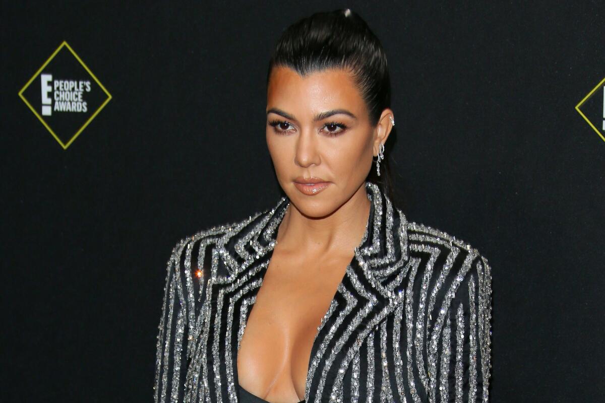 Kourtney Kardashian looks serious in a striped black-and-silver glittery blazer with slicked back hair