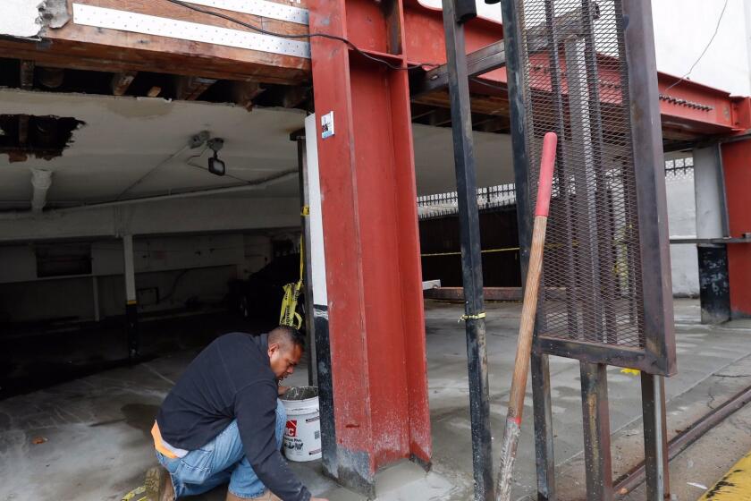 Kehl Tonga, a supervisor, adds cement to the base of a steel moment frame, to prevent water from making contact with the steel to prevent rust. The moment frame was installed to add structural support to the carport of a two story apartment building at 7050 Waring Ave in Los Angeles that is undergoing an earthquake retrofit.