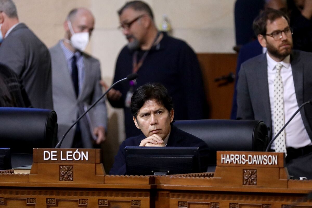 Kevin de León is seen sitting on the rostrum at the city council chamber with his hands folded under his chin.