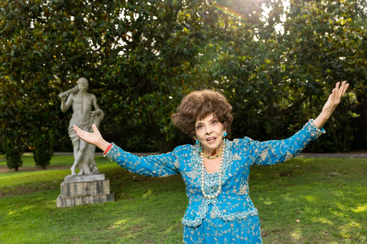 Gina Lollobrigida stands outdoors with her arms outstretched.