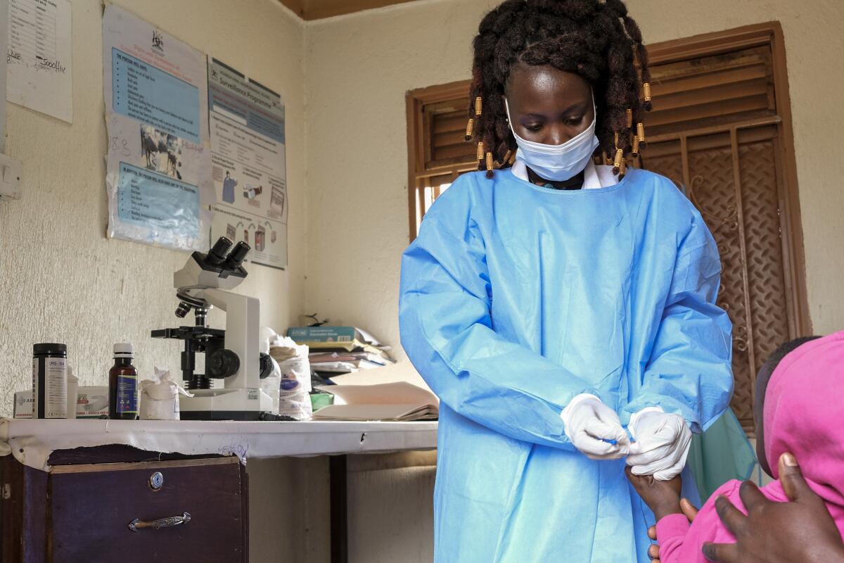 A medical lab assistant takes a blood sample from a toddler at a Uganda clinic.
