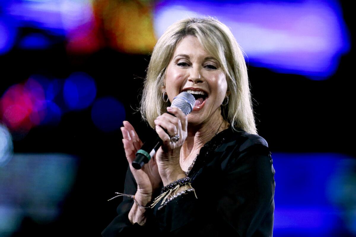 A woman smiles and performs onstage with a microphone