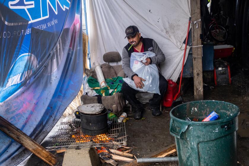 Los Angeles, CA - February 24: It's raining, cold, and windy Reynaldo Roman, 39, is trying to stay dry as he cooks a pot of beans in his makeshift home on Friday, Feb. 24, 2023, in Los Angeles, CA. Paul Avila gave him some new clothing. (Francine Orr / Los Angeles Times)