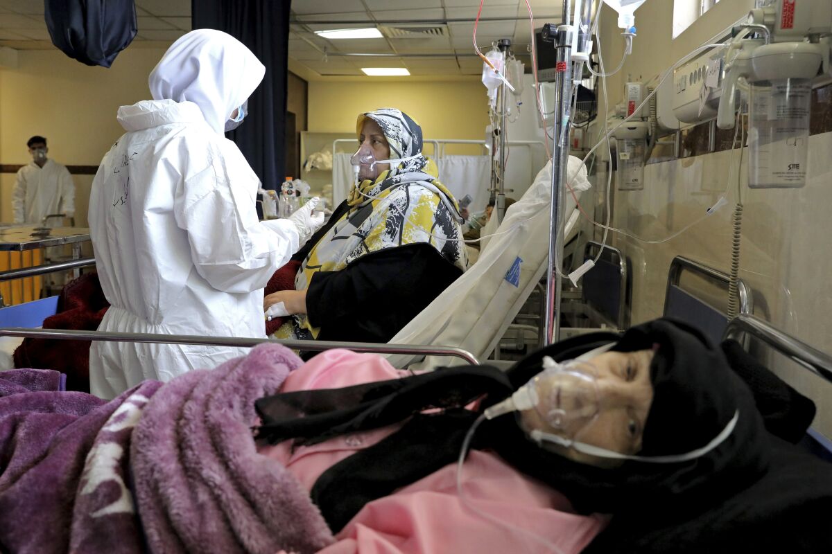 Patients lie in beds attended by caretakers in protective clothing