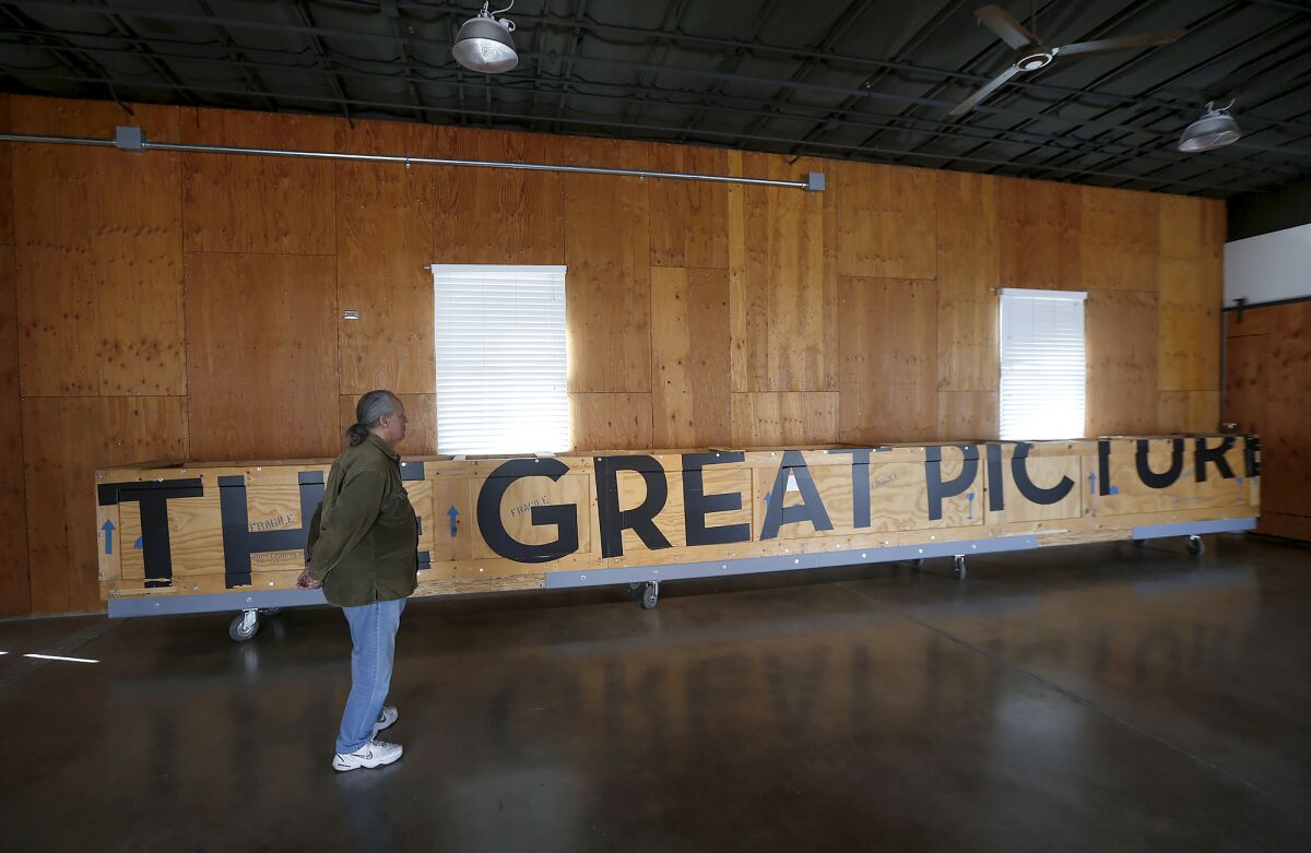 Clayton Spada stands next to a crate labeled "The Great Picture."