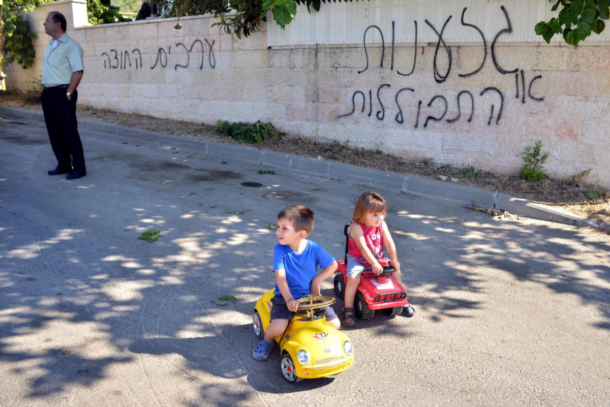 Children play near a wall in the Arab Israeli village of Abu Gosh defaced with graffiti reading, "Racism or assimilation" and "Arabs out."