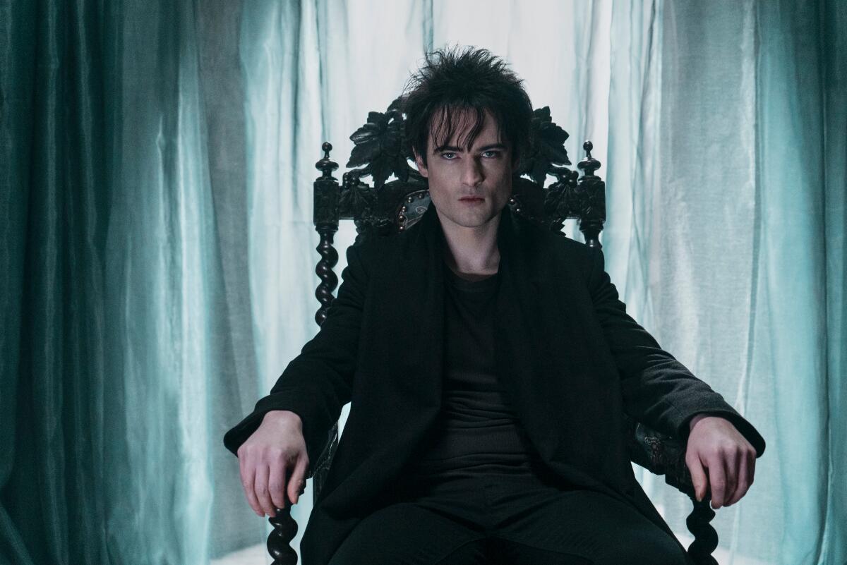 A man with disheveled black hair sits on an elaborate chair in a scene from "The Sandman."