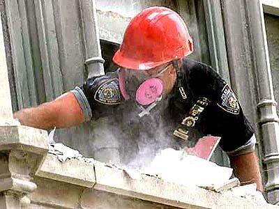 A New York Police detective works in an office window ledge near ground zero, searching for evidence in the debris.